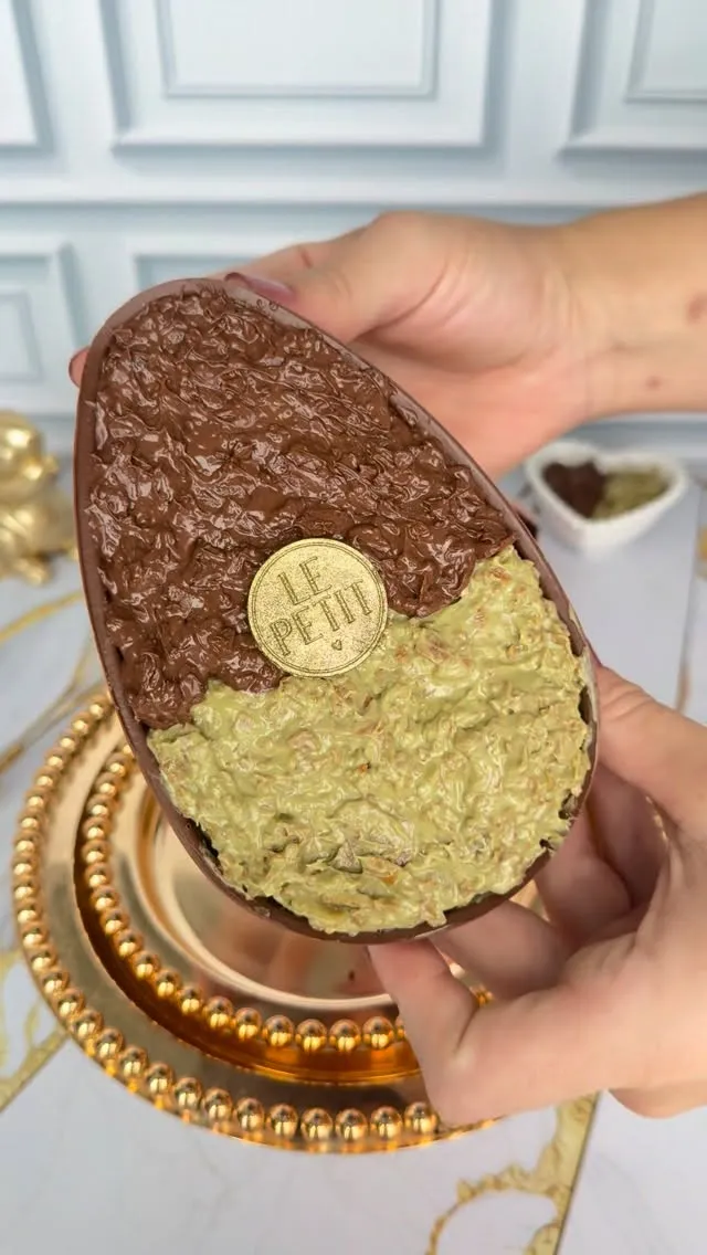 Metade de ovo de chocolate recheado, uma face de chocolate crocante e a outra de creme claro, com o selo dourado Le Petit no meio.
