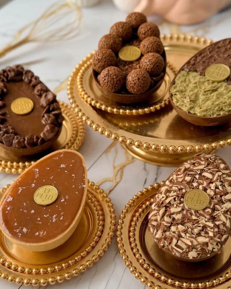 Cinco ovos de colher da Le Petit sobre bandejas douradas em uma bancada de mármore, cada um lacrado com o selo dourado da casa.